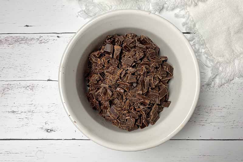 Horizontal image of finely chopped chocolate in a white bowl.