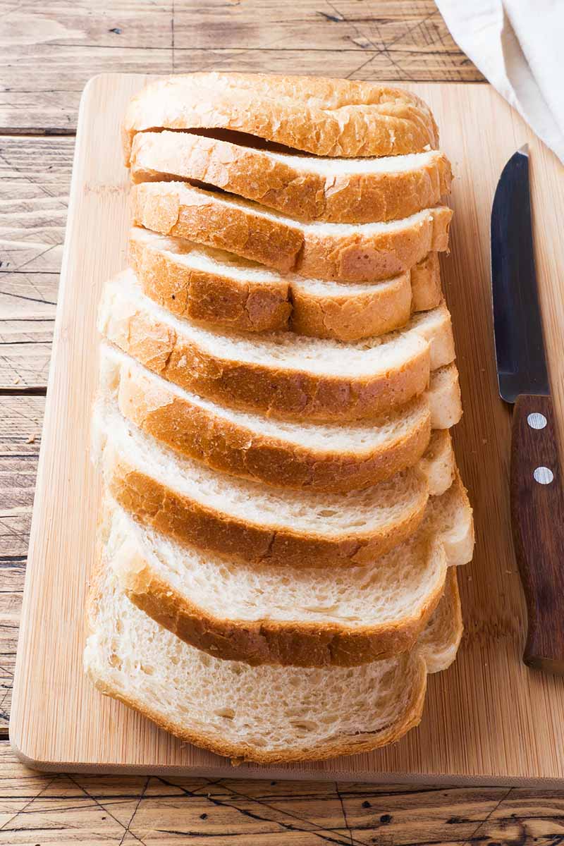 Vertical image of thick slices of white bread on a wooden cutting board next to a knife.