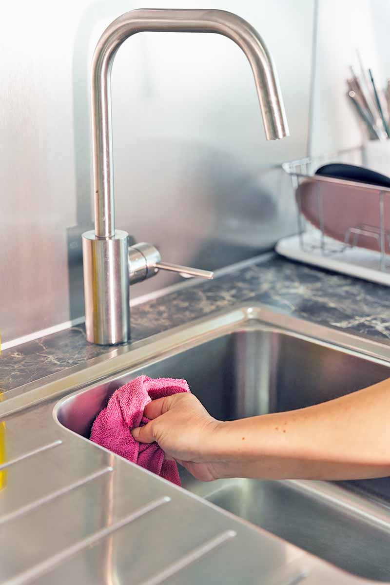 Vertical image of a hand wiping down a sink with a rag.