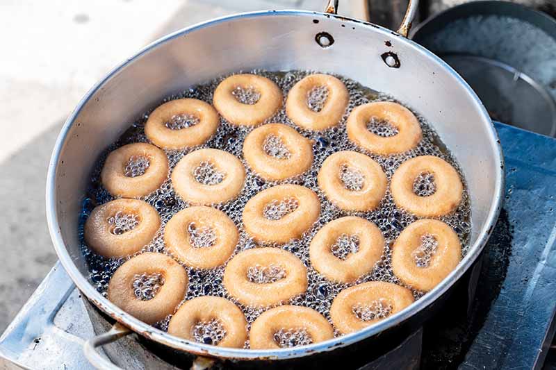 Horizontal image of cooking doughnuts in a large pot.