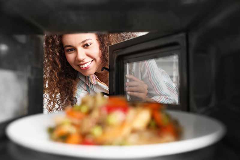 Horizontal image of a woman watching food being heated.