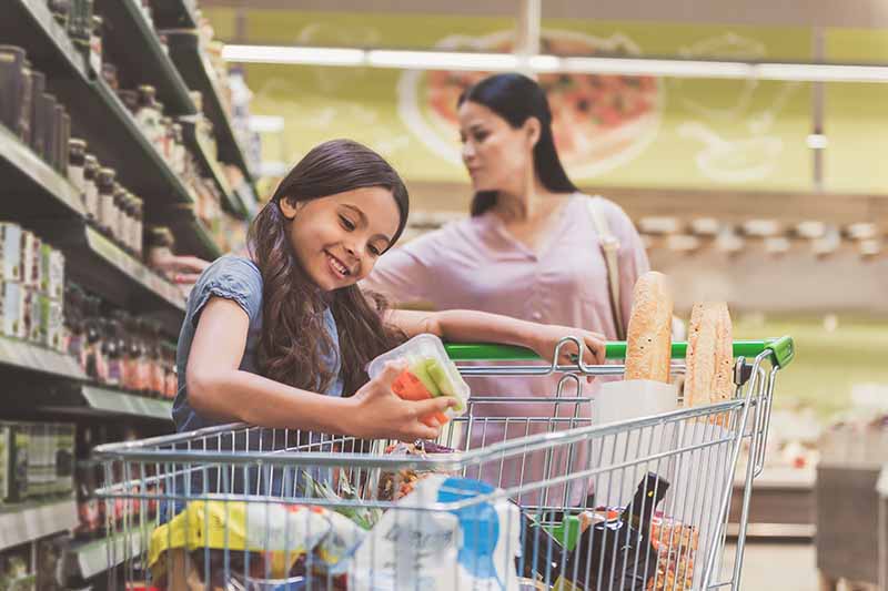 Horizontal image of a mom and daughter grocery shopping together.