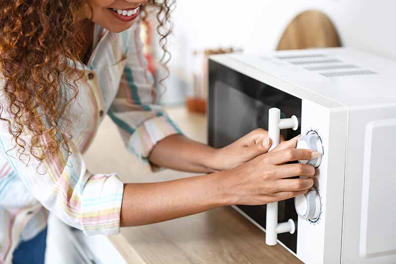 Horizontal image of a woman adjusting the knobs of a kitchen appliance on the countertop.