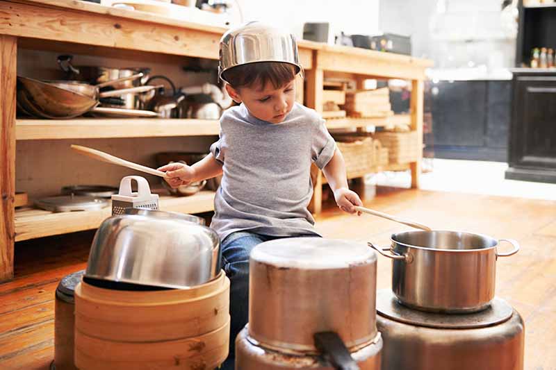 Horizontal image of a child playing drums on cooking tools.