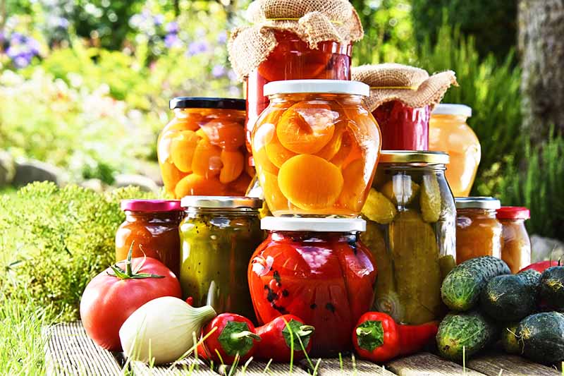 Horizontal image of stacks of preserved pickles and fruits on a wooden table.