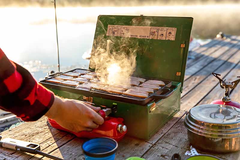 Horizontal image of a man cooking while on a dock next to the water.