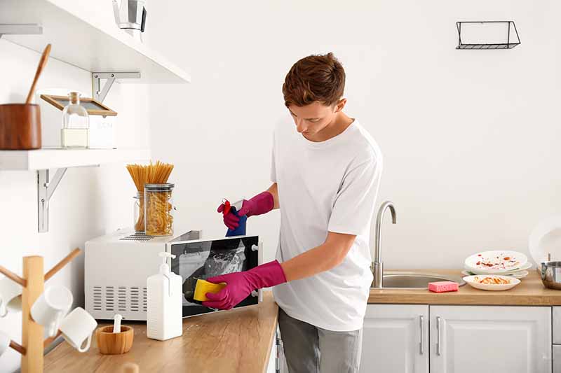 Horizontal image of a young man cleaning the kitchen area.