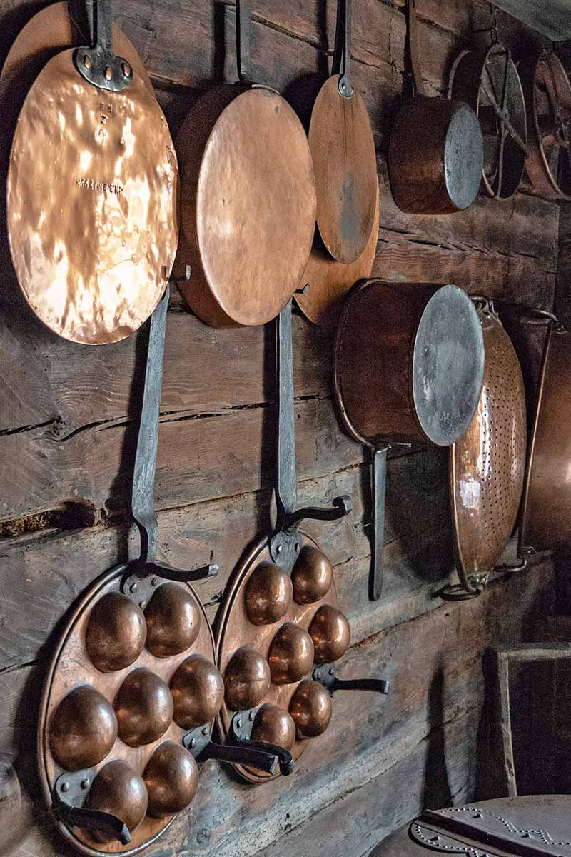 Vertical image of a wooden wall display with vintage copper cooking utensils.