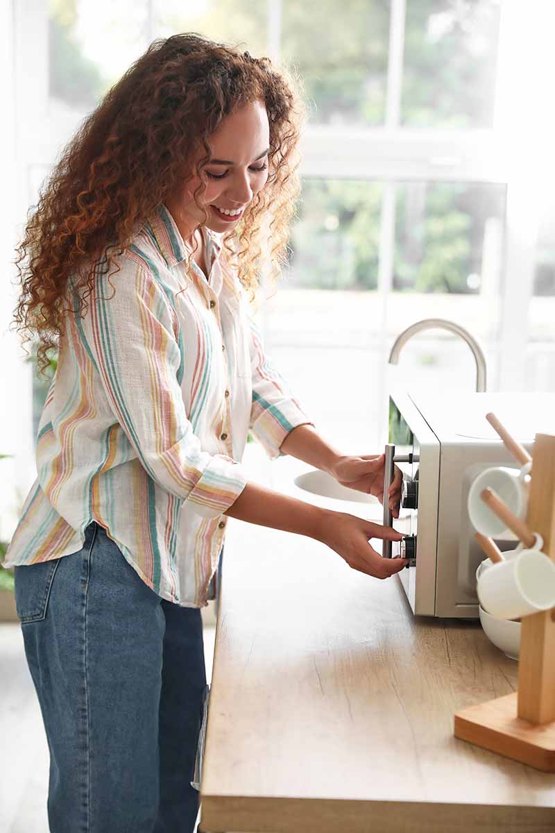 Vertical image of a woman heating food in an appliance.