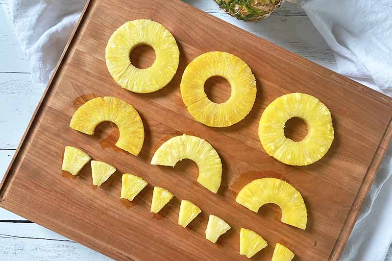 Horizontal image of rings, half rings, and chunks of fresh fruit on a wooden cutting board.