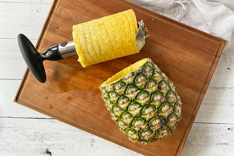 Horizontal image of a successfully cored whole pineapple on a wooden cutting board using a coring tool.