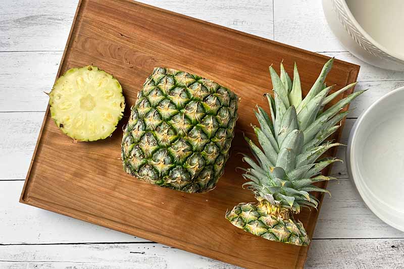 Horizontal image of a pineapple with the bottom and top removed on a wooden cutting board.