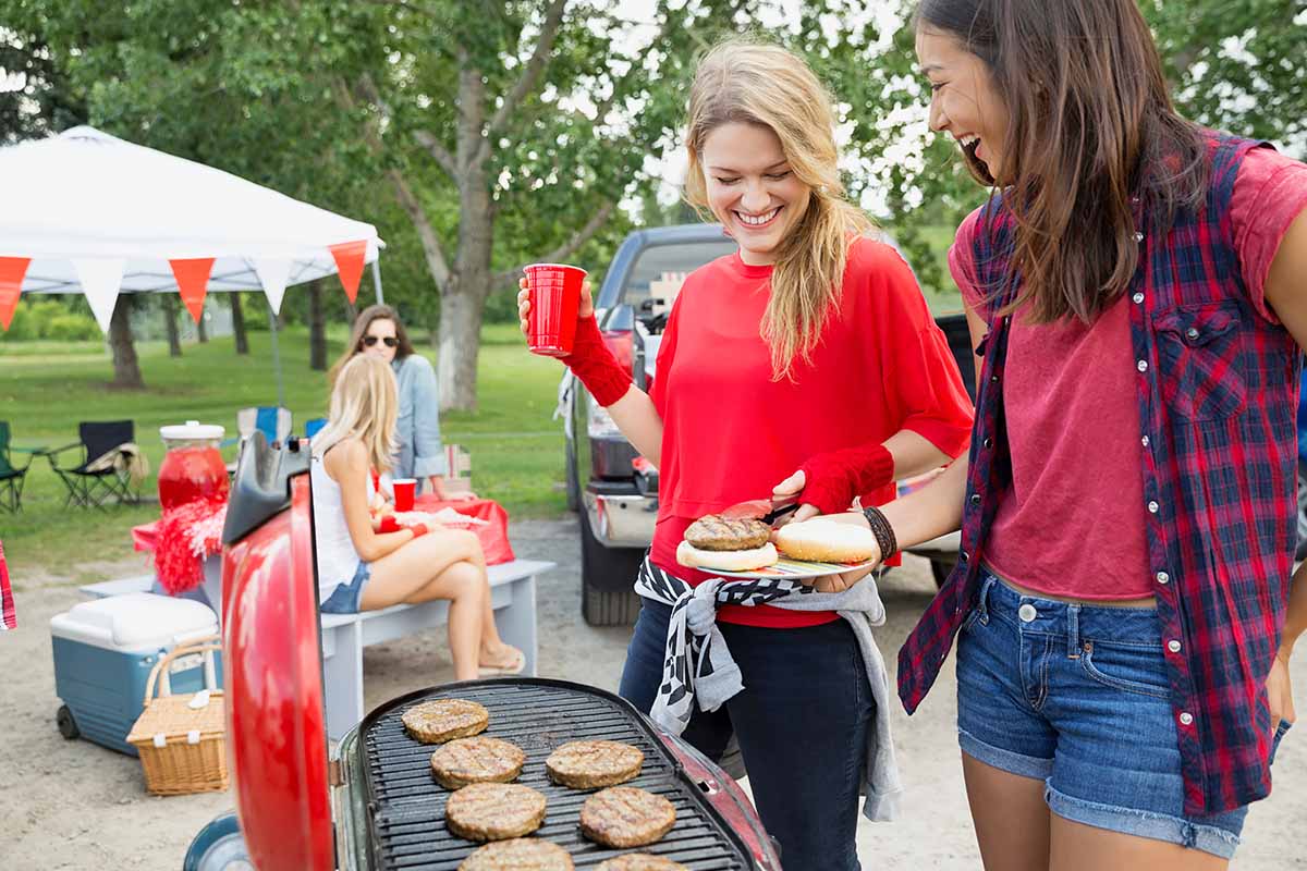 Horizontal image of women preparing burgers on a barbecue.