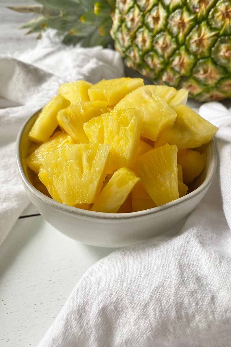 Vertical image of chunks of pineapple in a small white bowl.