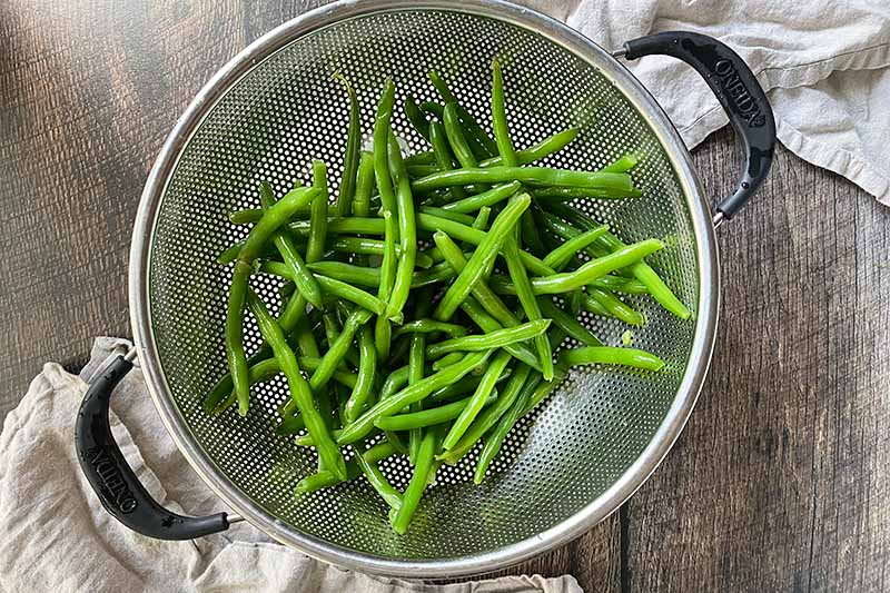 Horizontal image of draining blanched green beans in a colander.