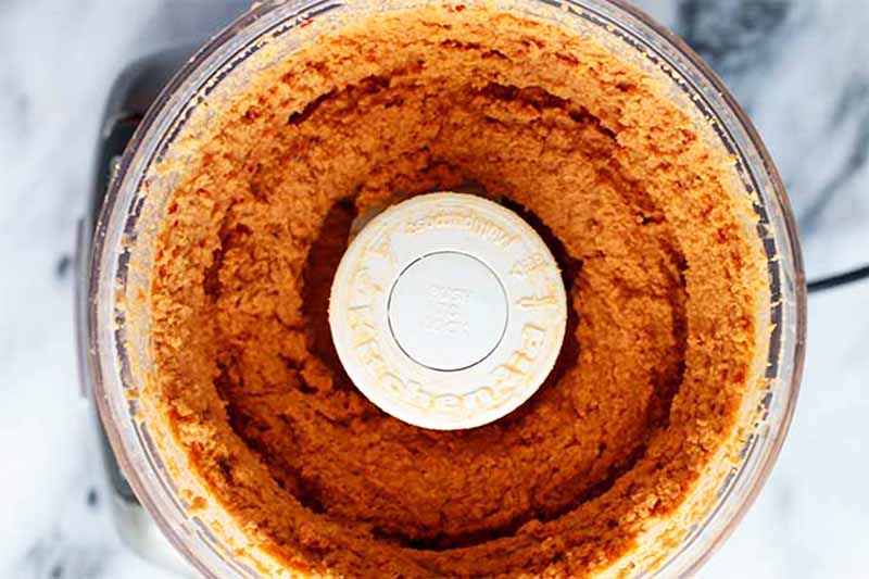 Horizontal image of a pureed light red mixture in a food processor.