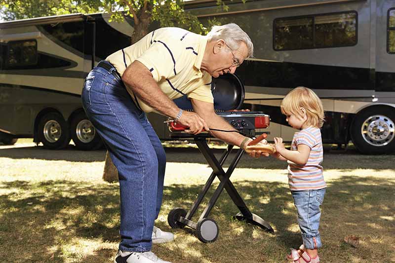 Horizontal image of a man handing a child a hotdog at a campsite.