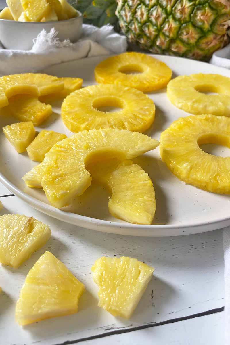 Horizontal image of cubes, half rings, and whole rings of a fresh yellow fruit on a white plate.
