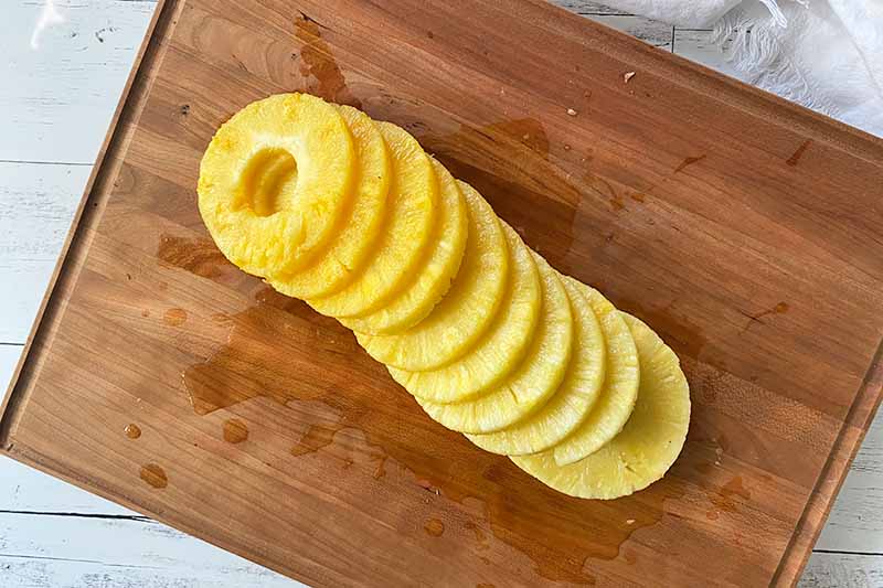 Horizontal image of rings of fresh pineapple on a wooden cutting board.