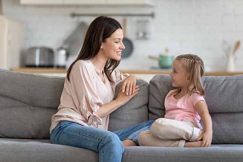 Horizontal image of a mom talking to her daughter on the couch.