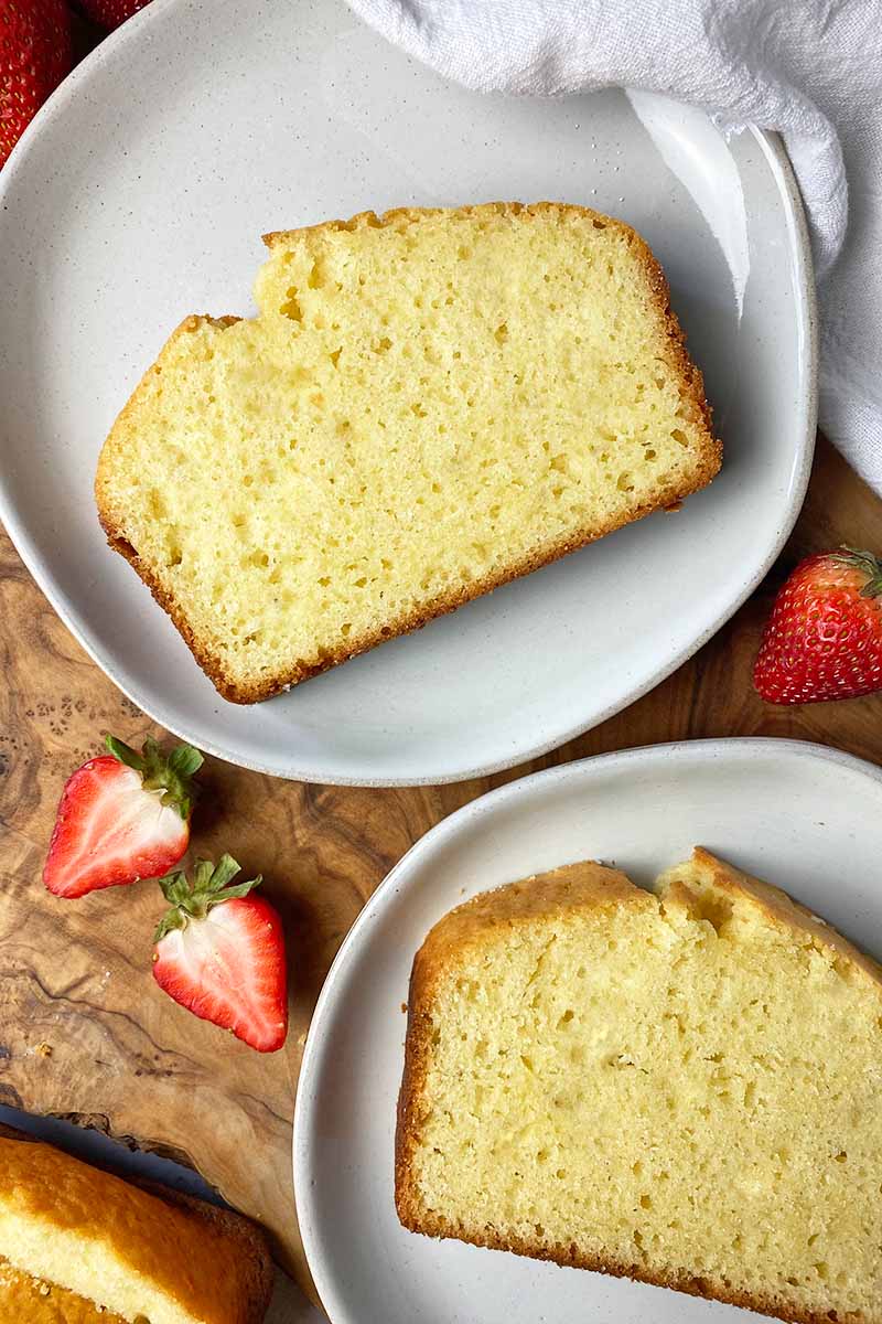 Vertical image of slices of a loaf cake on white plates next to strawberries.