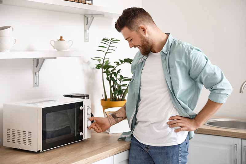 Horizontal image of a man heating food in the microwave.