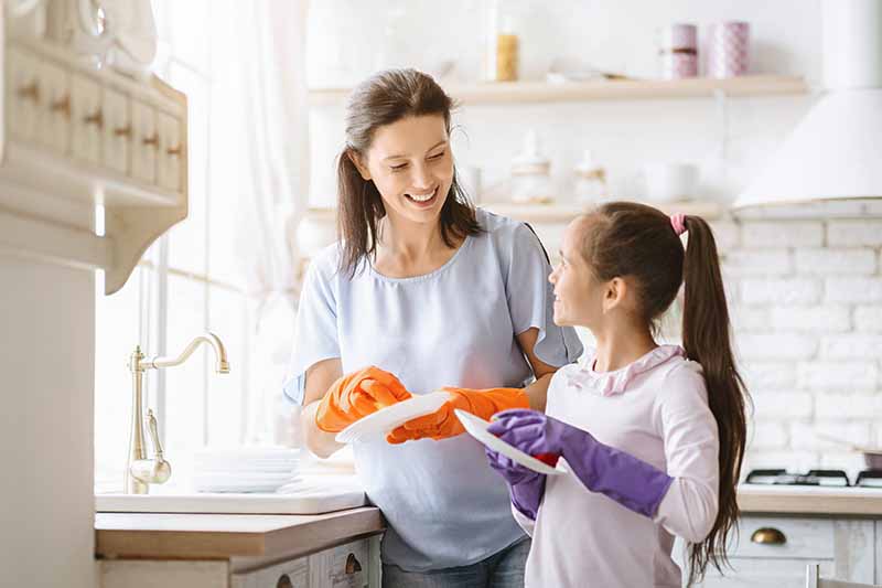 Horizontal image of a mother and daughter cleaning dishes together.