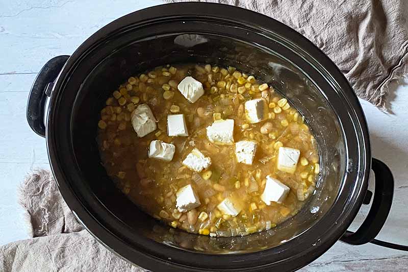 Horizontal image of a stew in a black ceramic insert topped with cubes of cream cheese.