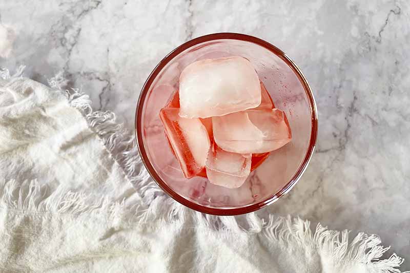 Horizontal image of ice cubes and a pink liquid in a cup.