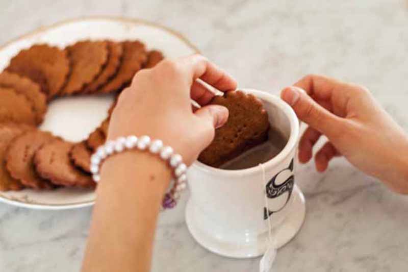 Horizontal image of a hand dipping a cookie in a mug of coffee.