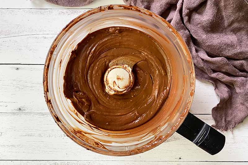 Horizontal image of a cocoa-flavored creamy mixture in a food processor.