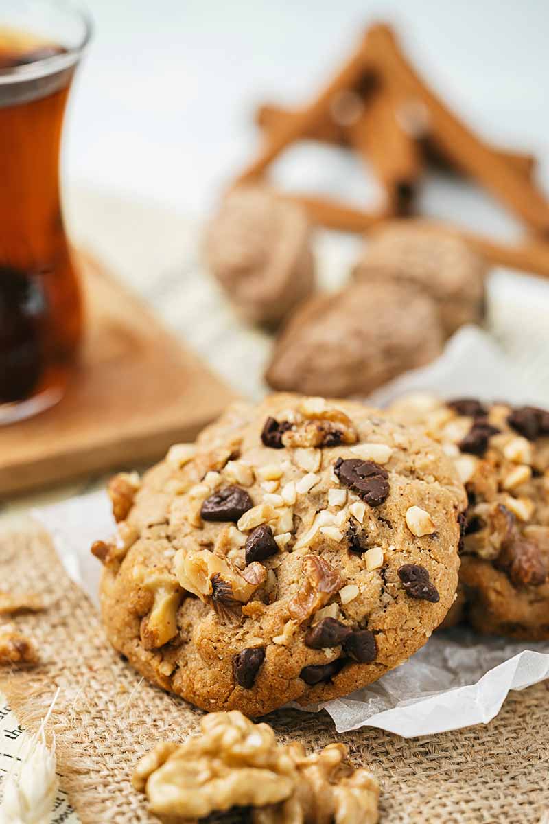 Vertical image of chunky cookies on burlap next to walnuts.