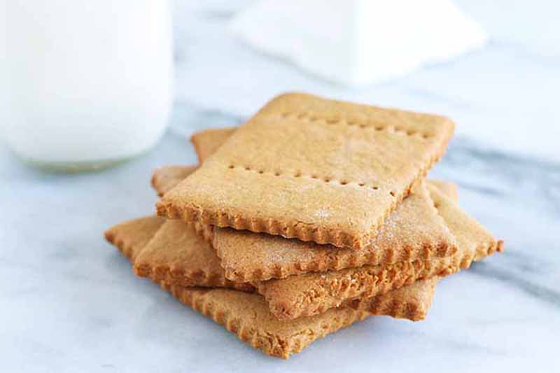 Horizontal image of a stack of homemade graham crackers next to a glass of milk.