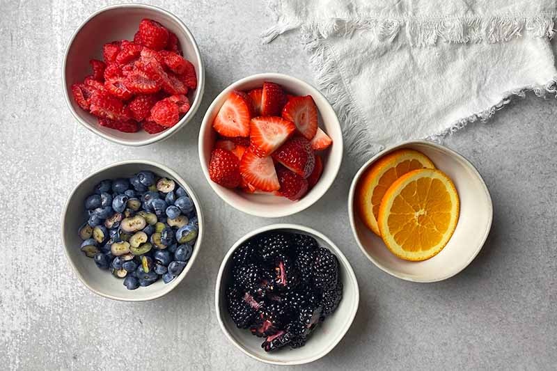 Horizontal image of white bowls, each filled with a prepped fresh fruit item.