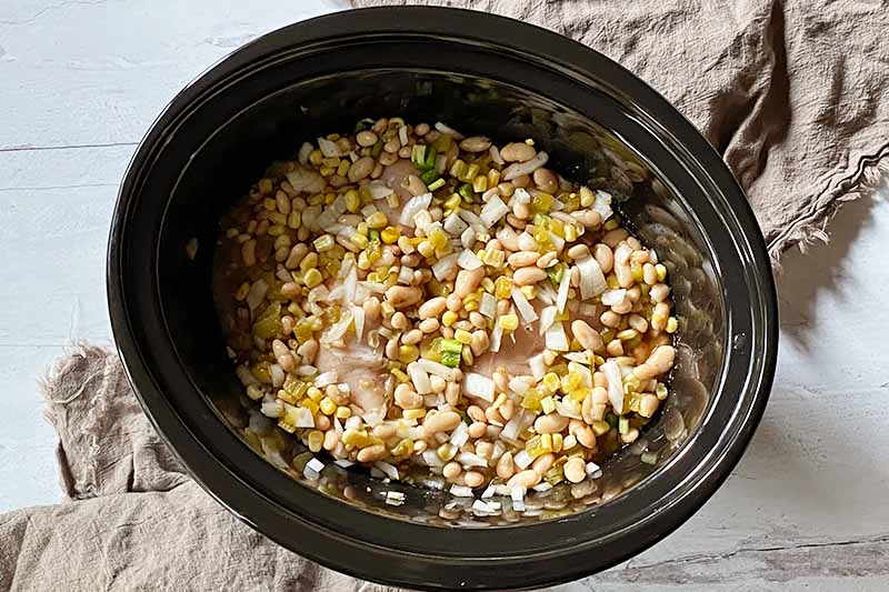 Horizontal image of a mix of beans, corn, onions, and aromatics in a ceramic insert.