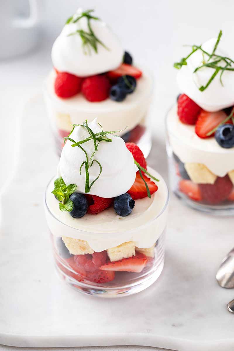 Vertical image of mini trifles with berries and whipped cream, with mint garnish.