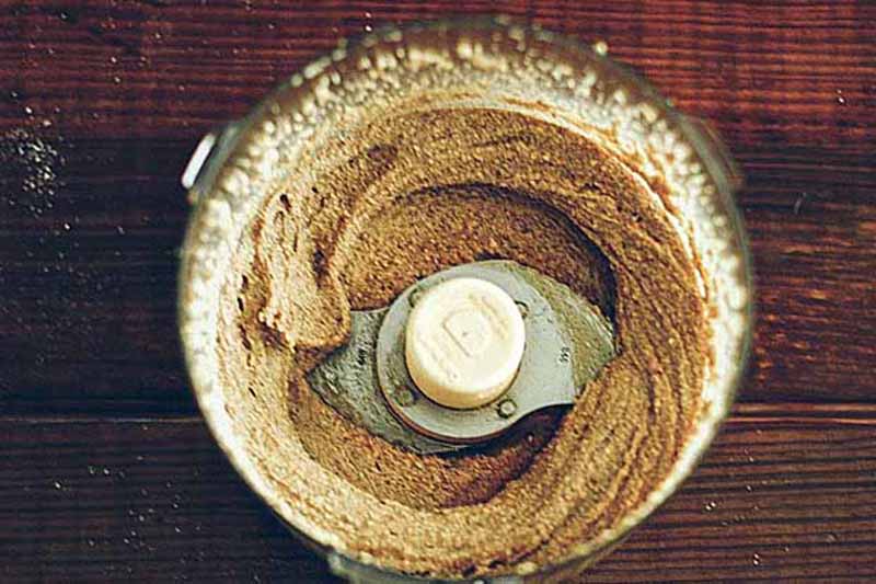 Horizontal image of a nut butter in a food processor on a wooden table.