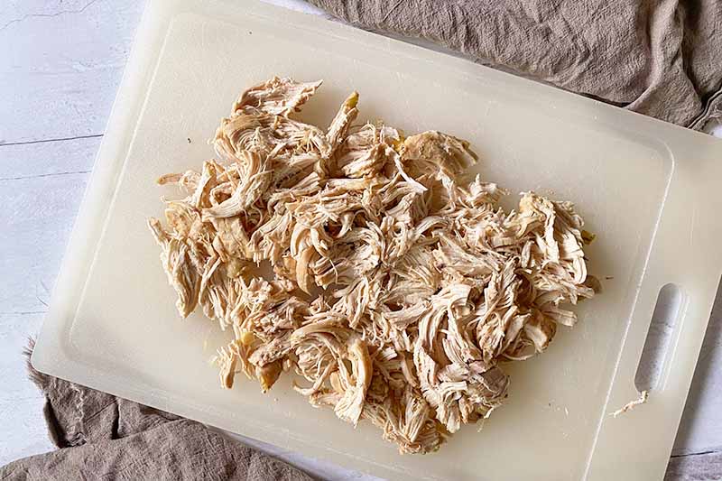 Horizontal image of shredded poultry on a cutting board.