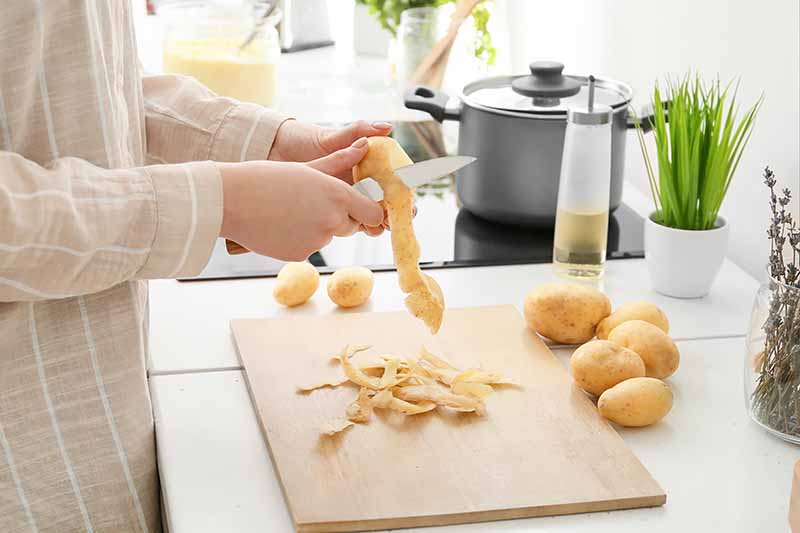 Horizontal image of peeling raw potatoes on a wooden cutting board on a table .