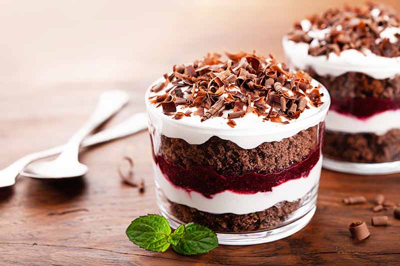 Horizontal image of mini chocolate and whipped cream trifles with a cherry layer on a wooden surface.
