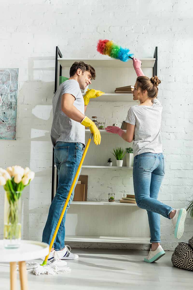 Vertical image of a man and woman cleaning a bookshelf together.