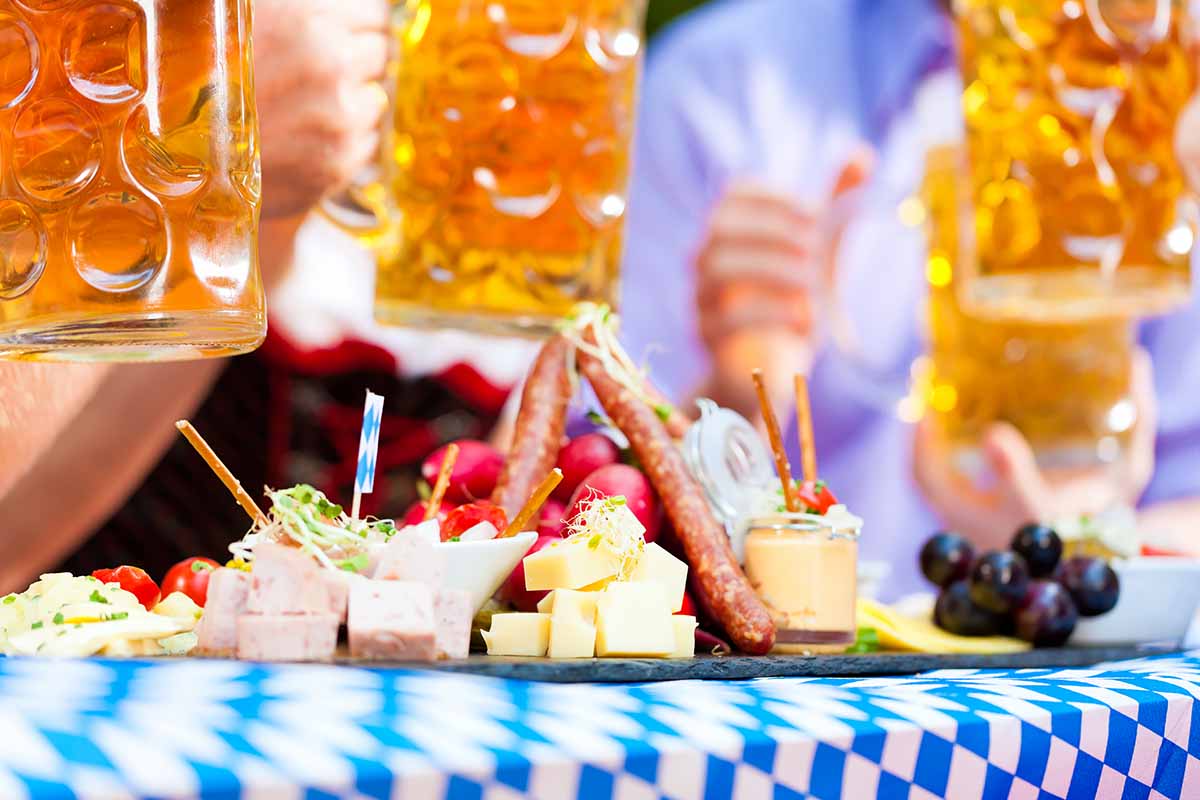 Horizontal image of people holding large glass steins over a decorated table with an assorted charcuterie board.