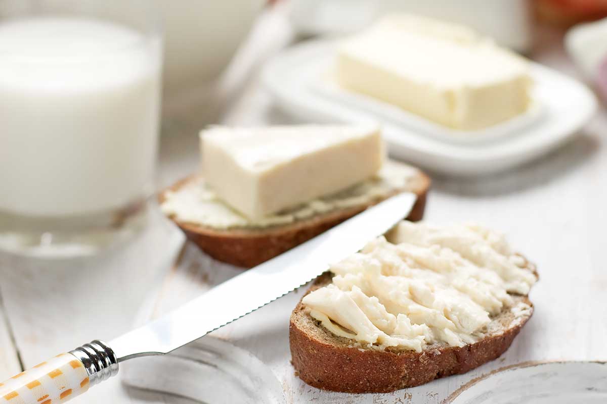 Horizontal image of slices of bread topped with a thick white spread next to a glass of milk and knife.