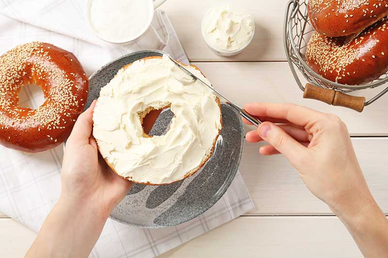 Horizontal image of covering half of a bagel with a very thick, white spread.