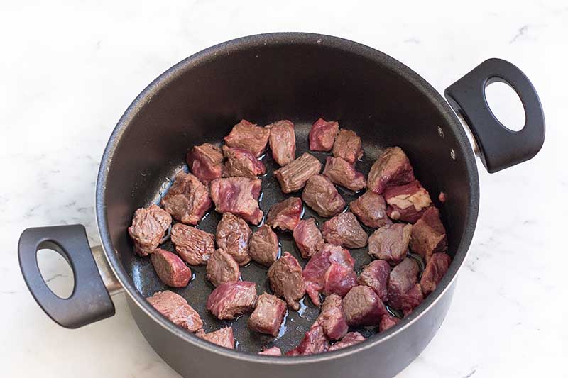 Horizontal image of browning cubes of raw meat in a large pot.