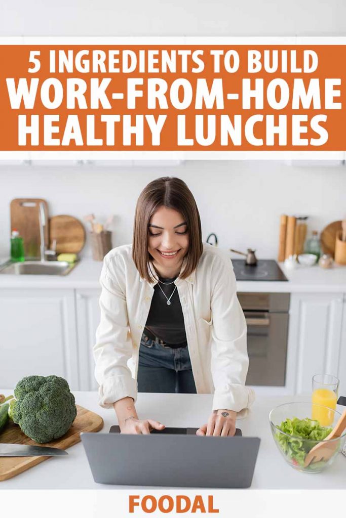 Vertical image of a woman working on hr laptop in the kitchen next to broccoli and mixed greens.