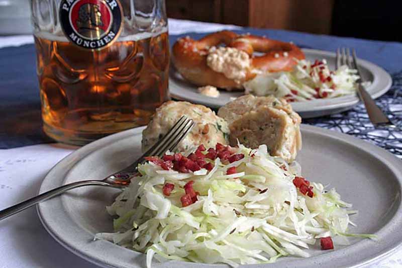 Horizontal image of a plate of cabbage slaw in front of dumplings next to a stein of beer.