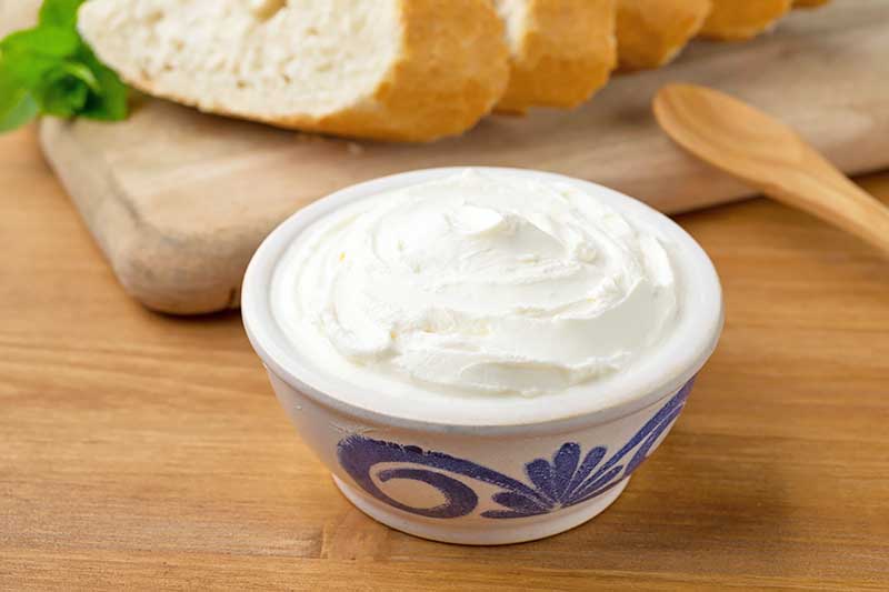 Horizontal image of fromage blanc in a porcelain bowl on a wooden table in front of sliced bread.