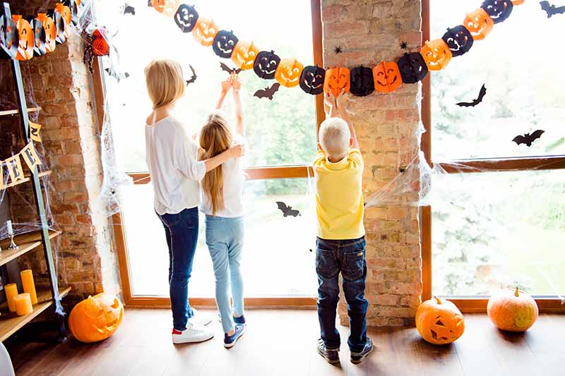 Horizontal image of a family putting up fall-themed decorations on a window in the living room.