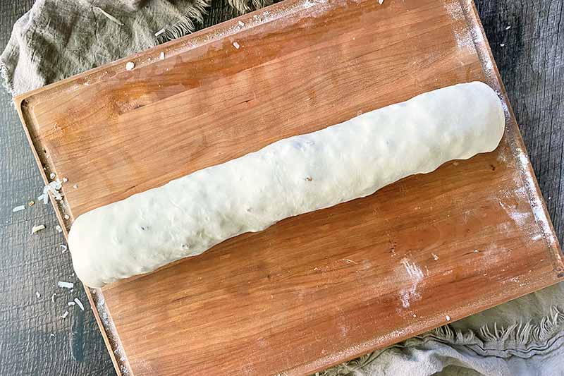 Horizontal image of an unbaked dough roll on a wooden cutting board.